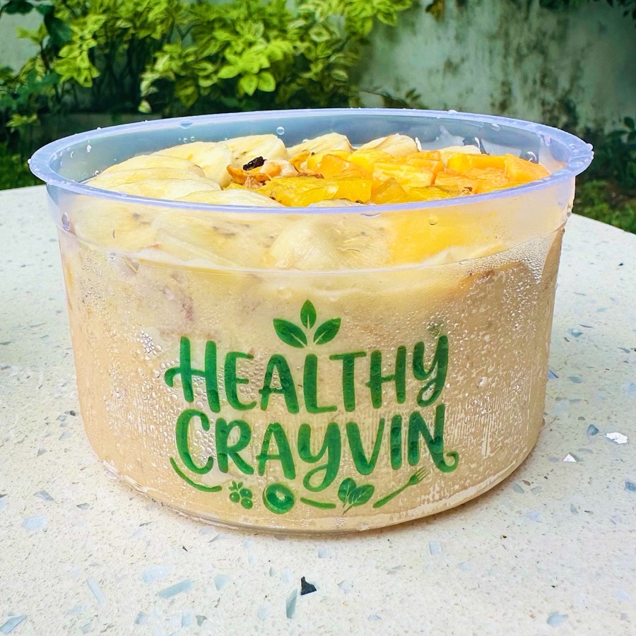 Sunshine bowl in a Healthy Crayvin cup, golden base topped with banana slices and mango